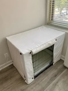 a dog crate with a white cover on it's side in front of a window