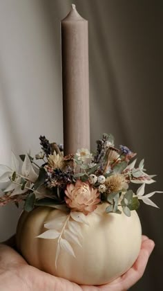 a hand holding a white pumpkin with flowers and a candle in it's center