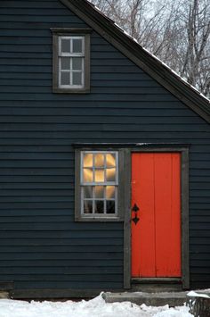 a red door sits in the window of a blue house with snow on the ground