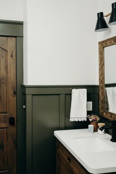 a white sink sitting under a bathroom mirror next to a wooden door and wall mounted light