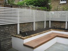 a wooden bench sitting in the middle of a garden next to a brick wall and fence