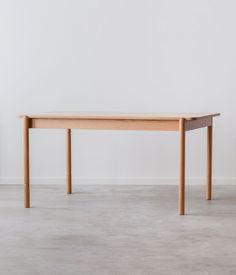 a wooden table sitting on top of a cement floor next to a white wall and potted plant