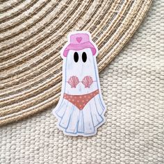 a sticker depicting a ghost wearing a pink hat and undershirt with seashells on it