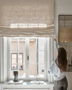 a woman standing in front of a window with her arms up and looking out the window