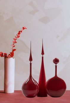 three red vases sitting on top of a table next to a white vase with flowers in it