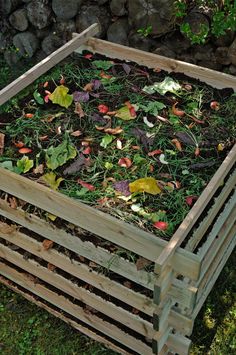 a wooden box filled with lots of green plants and dirt on top of the ground