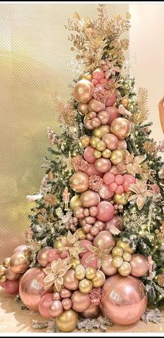 a woman standing next to a christmas tree with pink and gold ornaments on it's sides