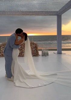 a bride and groom kissing in front of an ocean view at their wedding ceremony with the sun setting behind them