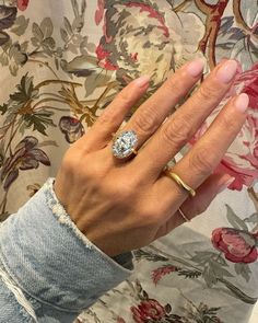 a woman's hand with a diamond ring on top of her left hand, in front of a floral wallpaper