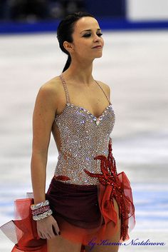 a female figure skating on the ice in a short dress with red and white accents