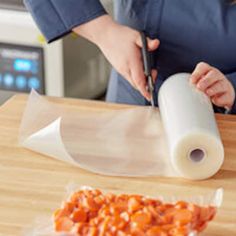 a woman cutting up food on top of a wooden table next to a roll of paper