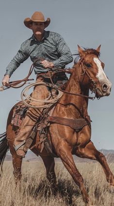 a man riding on the back of a brown horse across a dry grass covered field