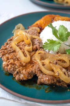 a blue plate topped with meat covered in sauce and onions next to rice on top of a table