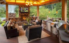 an outdoor living area with fireplace, grill and television on top of the roof over looking trees