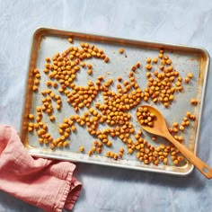 a baking pan filled with chickpeas on top of a blue table cloth next to a wooden spoon