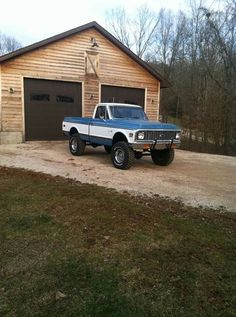 a blue and white truck parked in front of a wooden building with two garages