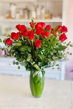 a green vase filled with red roses on top of a table