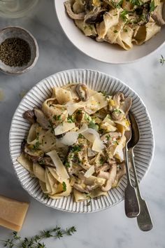 pasta with mushrooms and parsley in a white bowl on a marble countertop next to two bowls of seasoning