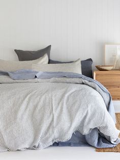 an unmade bed with blue and white linens in a small room next to a wooden dresser