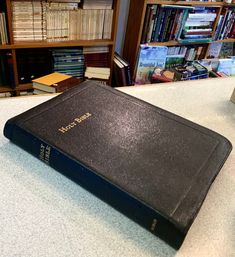 a large black book sitting on top of a table next to a bookshelf