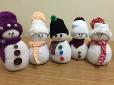 four snowmen wearing hats and scarves are lined up on a wooden table top