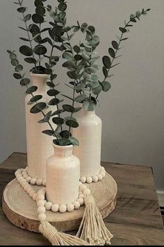 two white vases with green plants in them on a wooden table next to each other