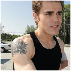 a man with a flower tattoo on his arm standing in front of a parking lot