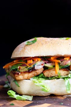 a chicken sandwich with lettuce, carrots and other toppings on a cutting board