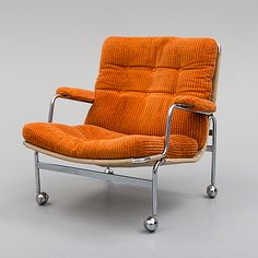 an orange chair sitting on top of a white floor next to a metal frame and wheels