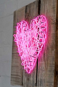 a neon pink heart is mounted on a wooden wall with string attached to the side