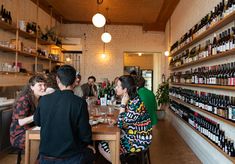 several people sitting at a table with wine bottles on the wall behind them and shelves in the background