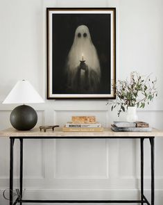 a table topped with a lamp next to a painting and a vase filled with flowers