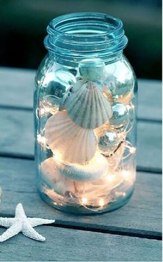 a glass jar filled with shells and lights on top of a wooden table next to a starfish