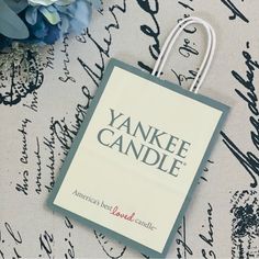 a paper bag with the name yankee candle on it sitting next to some blue flowers