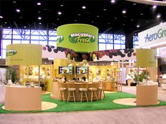 a booth with tables and chairs in front of a large screen display at a trade show