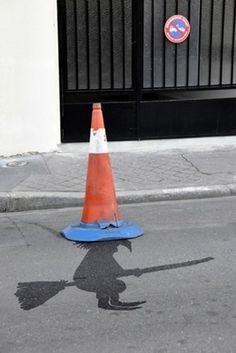 an orange traffic cone sitting on the side of a road next to a blue cone