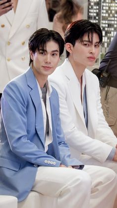 two young men in suits sitting next to each other on white couches at an event