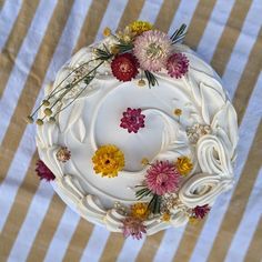 a white cake with flowers on it sitting on a striped tablecloth covered table cloth