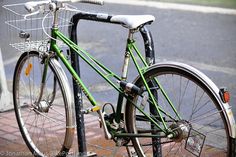 a green bike parked on the side of a street next to a sidewalk with red bricks