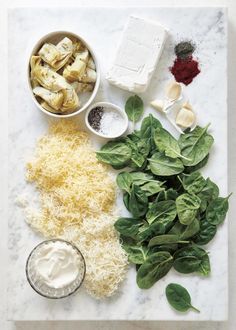 spinach, artichokes, cheese and other ingredients laid out on a marble board