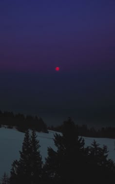 the sun is setting over some trees on a snowy hill with purple skies in the background