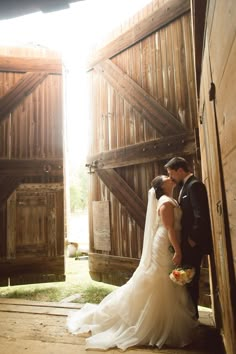 a bride and groom standing in front of an open barn door with the sun shining through