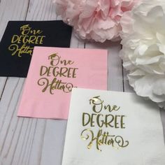 three paper napkins with gold lettering on them and pink flowers in the background,