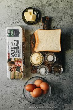 bread, butter, eggs and other ingredients are laid out on a counter top next to an egg carton