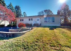 a house that is in the grass with trees and bushes on the side of it