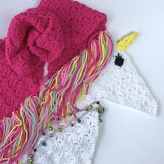 two crocheted unicorn scarfs on a white surface with one pink and one yellow