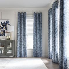 a living room with blue curtains and a white rug in front of a window that has an abstract painting on the wall