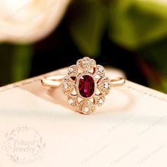 a red and white diamond ring sitting on top of a piece of paper next to flowers