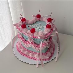 a pink and blue birthday cake with cherries on top