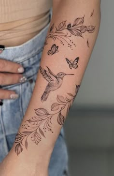 a woman's arm with a hummingbird and flowers tattoo on the left forearm